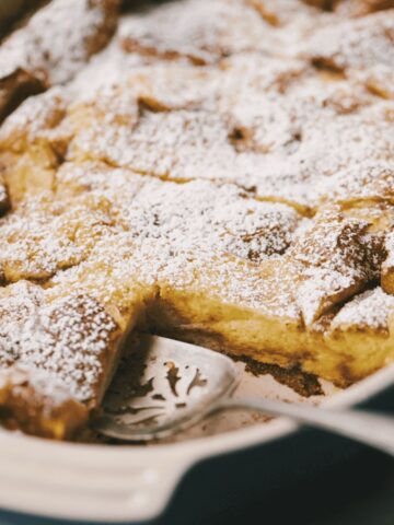 Brioche French toast in a casserole dish with a spoon, garnished with powdered sugar
