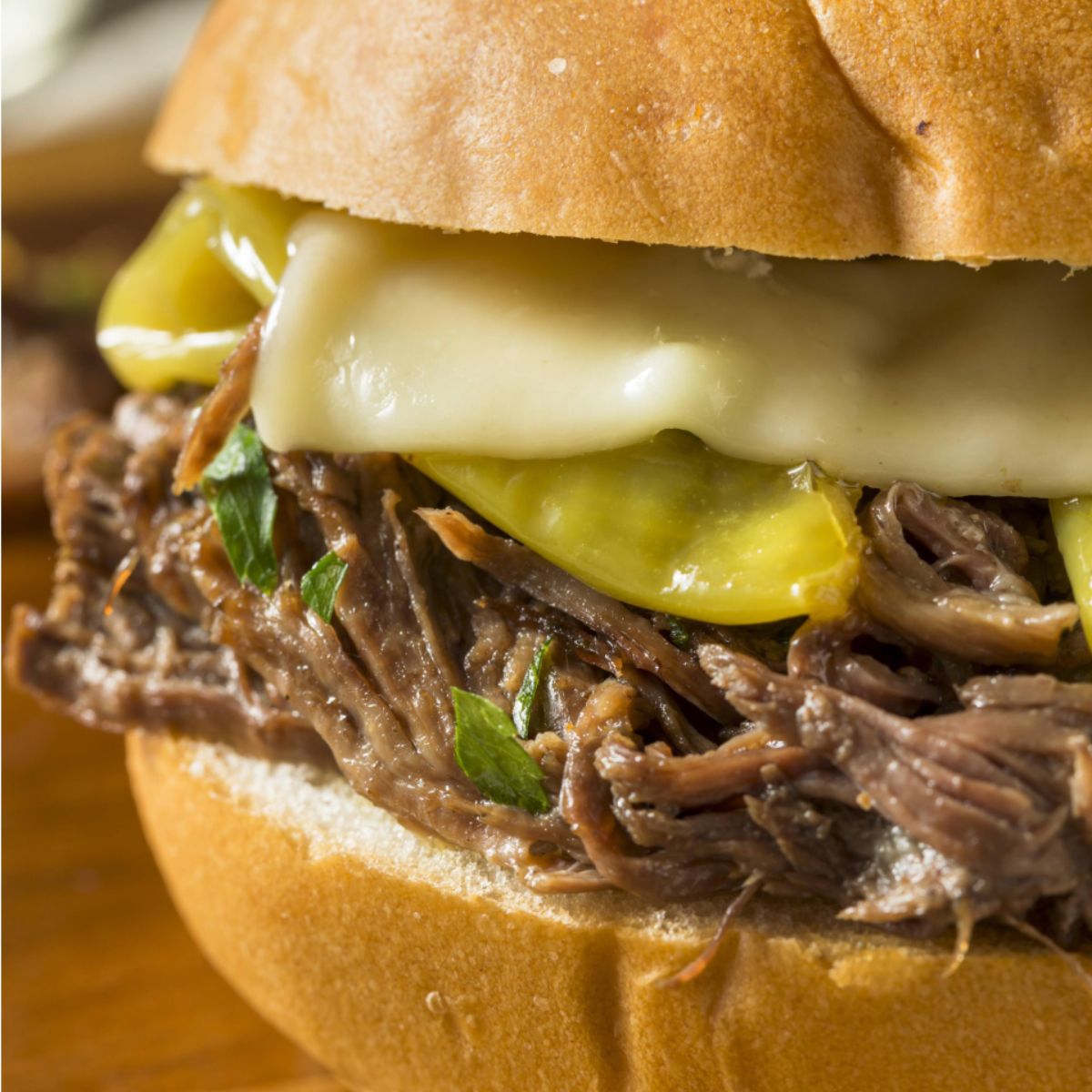 Close-up of a Mississippi pot roast slider on a bun, filled with tender shredded beef, sliced pepperoncini peppers, melted provolone cheese, and garnished with fresh parsley.