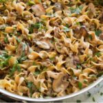 Close-up of a pan of creamy beef stroganoff: egg noodles coated in a savory mushroom and ground‑beef sauce, sprinkled with fresh parsley.