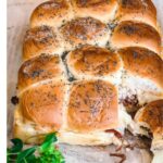 A picture of my corned beef sliders topped with poppy seeds on a wood, cutting board, garnished with greenery for St. Patrick's Day.