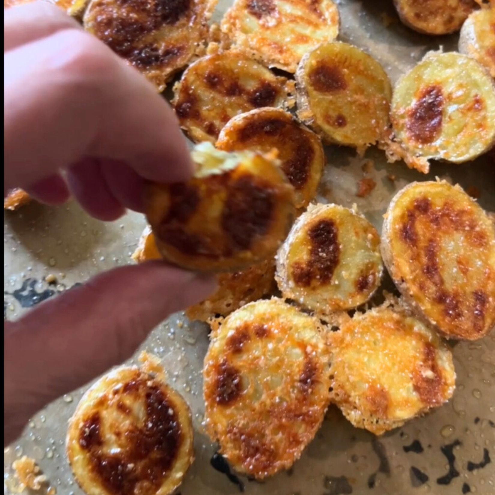 Garlic Parmesan crust, potatoes, with a hand showing the crispy side of the parmesan crusted potatoes