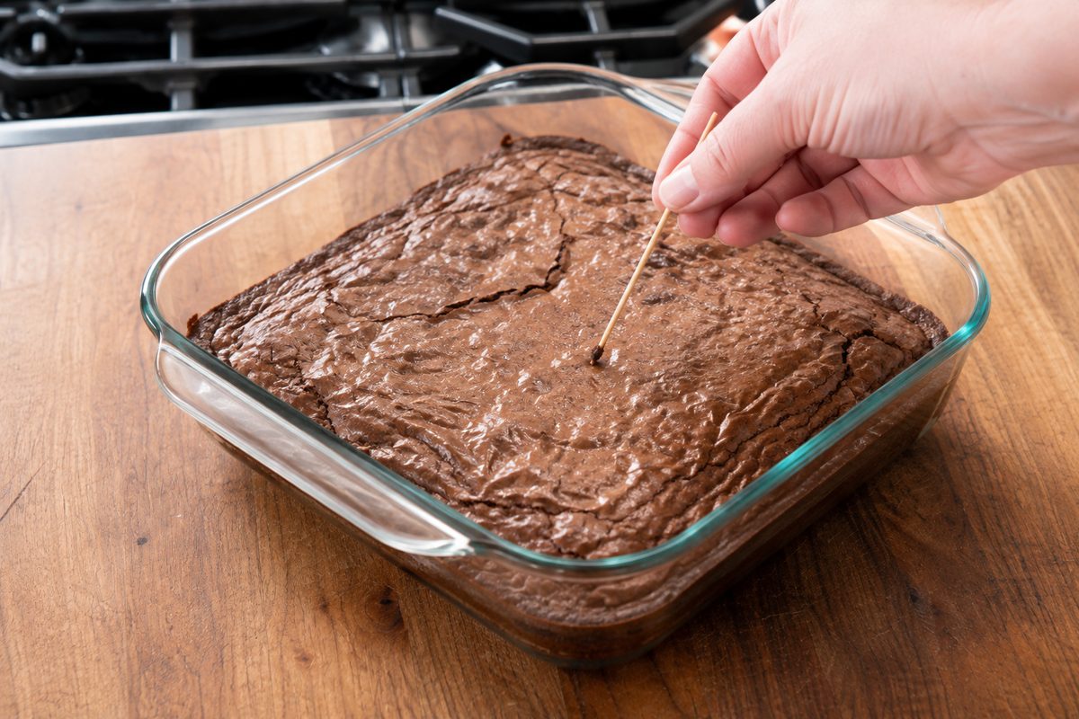 Toothpick checking baked brownies for moist crumbs in an 8x8-inch glass pan.
