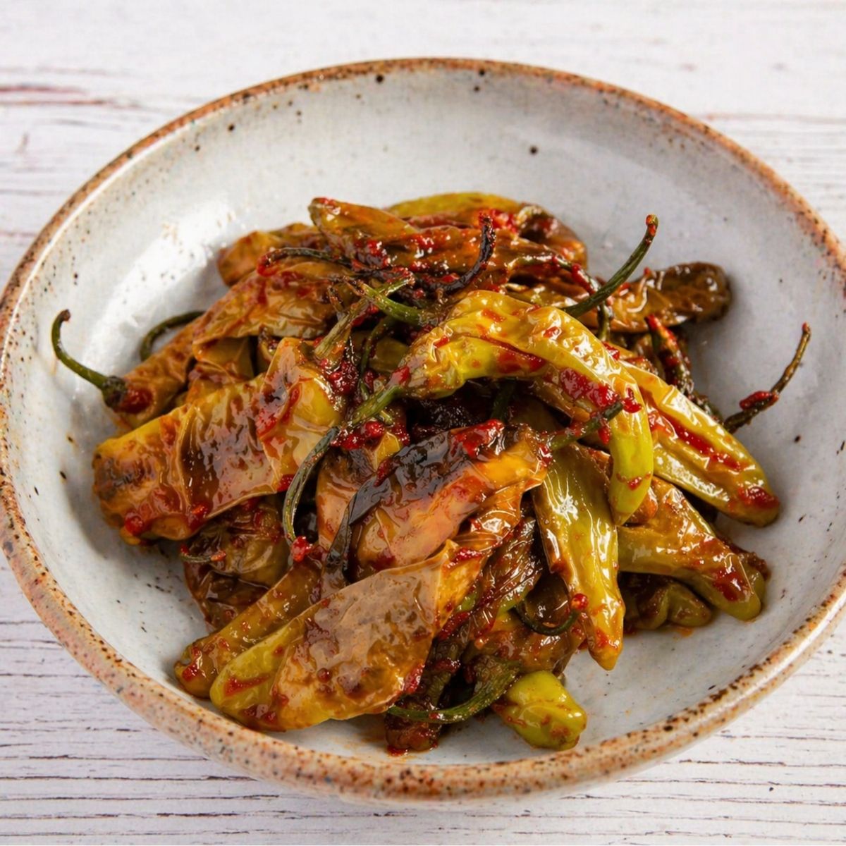 Shishito Pepper Recipe in a classic sauce and a white bowl of speckles on a white wood table.