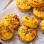 veggie egg bites stacked on parchment with vegetables and parsley garnish.