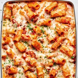Chicken Parmesan pasta bake and a casserole dish. With gooey melted cheese on top garnished with parsley.