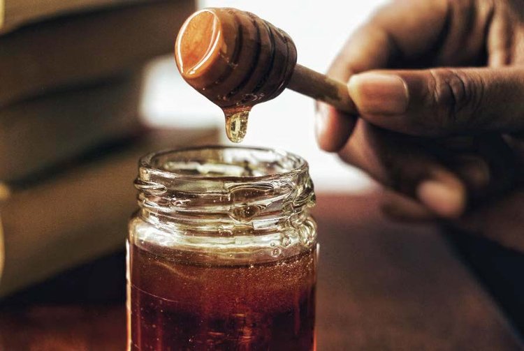 But honey in a mason jar with a honey dipper dripping slightly with a man's hand.