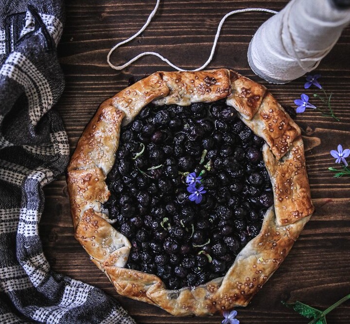A blueberry Galette or Crostata on a wood surface, with a blue and white dish towel, rustic crust and a spool of twine.