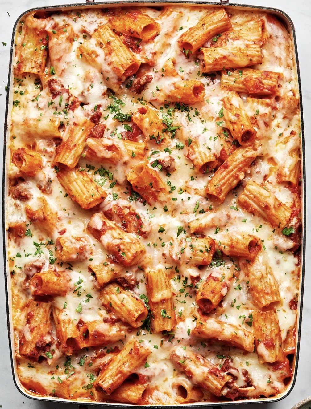 A casserole dish with chicken Parmesan baked pasta in it with a cheesy top marinara sauce, and garnished with parsley.