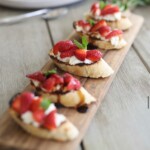 Sliced baguette topped with whipped cheese, fresh strawberry pieces, balsamic glaze, and mint leaves, arranged on a wooden serving board.