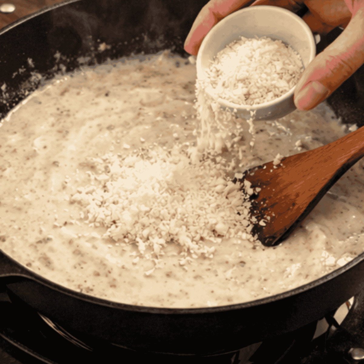Freshly grated parmesan cheese melting into simmering creamy parmesan sauce in skillet.