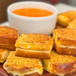 Mini grilled cheese sandwich sandwiches that are golden Brown with a cup of tomato soup sandwiches are stacked pie and look delicious.