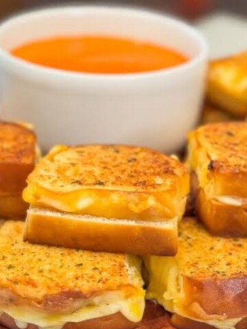 Mini grilled cheese sandwich sandwiches that are golden Brown with a cup of tomato soup sandwiches are stacked pie and look delicious.