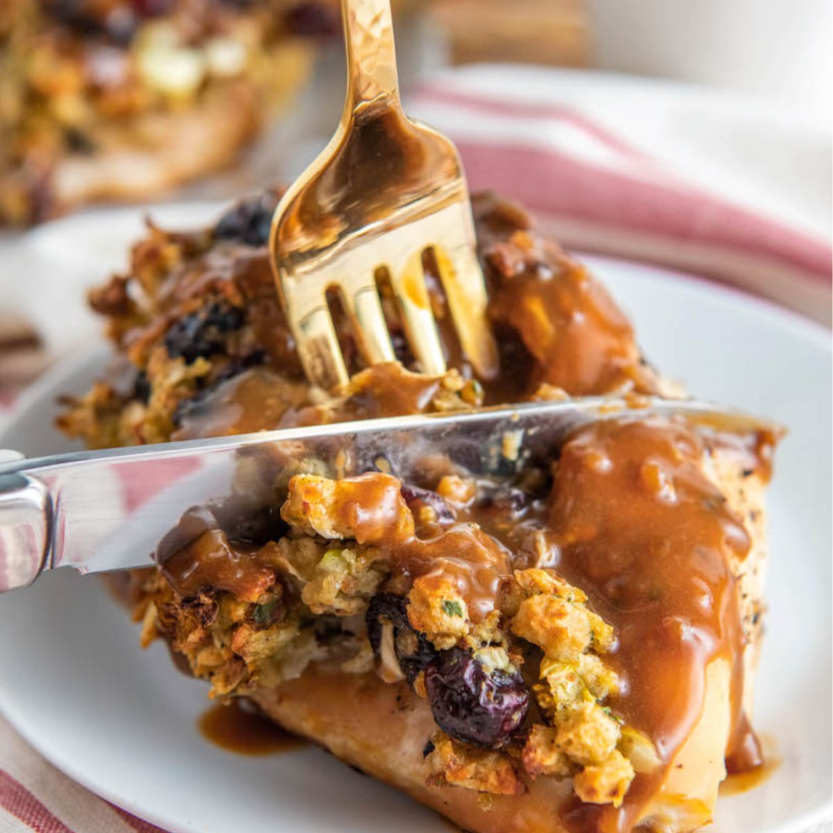 Chicken breast stuff with stuffing, smothered and gravy with a knife in for cutting it in half on a white plate