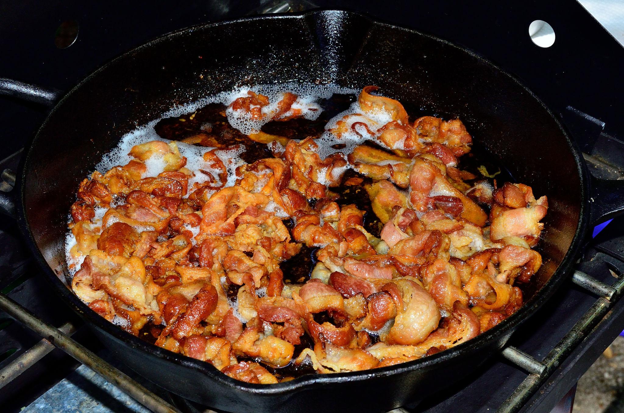 Crispy bacon cooking in skillet for baked potato soup.