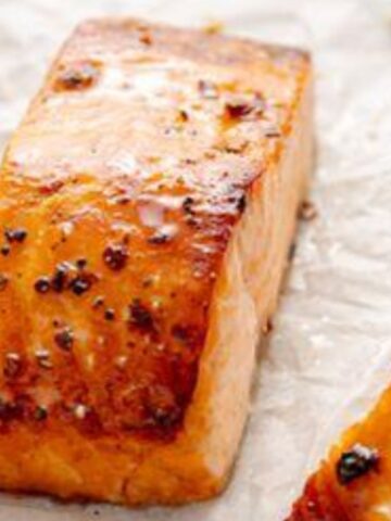 Broiled salmon fillet with golden top and flaky interior on parchment paper.