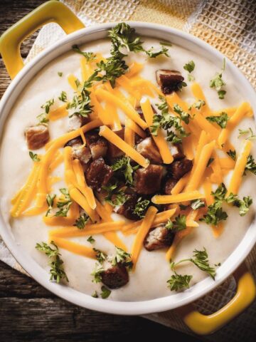 Creamy baked potato soup topped with shredded cheddar cheese, crispy bacon, and fresh parsley.