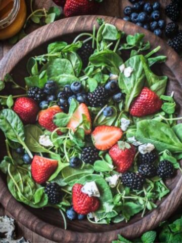 Mixed green salad with berries and cheese in a wooden bowl.