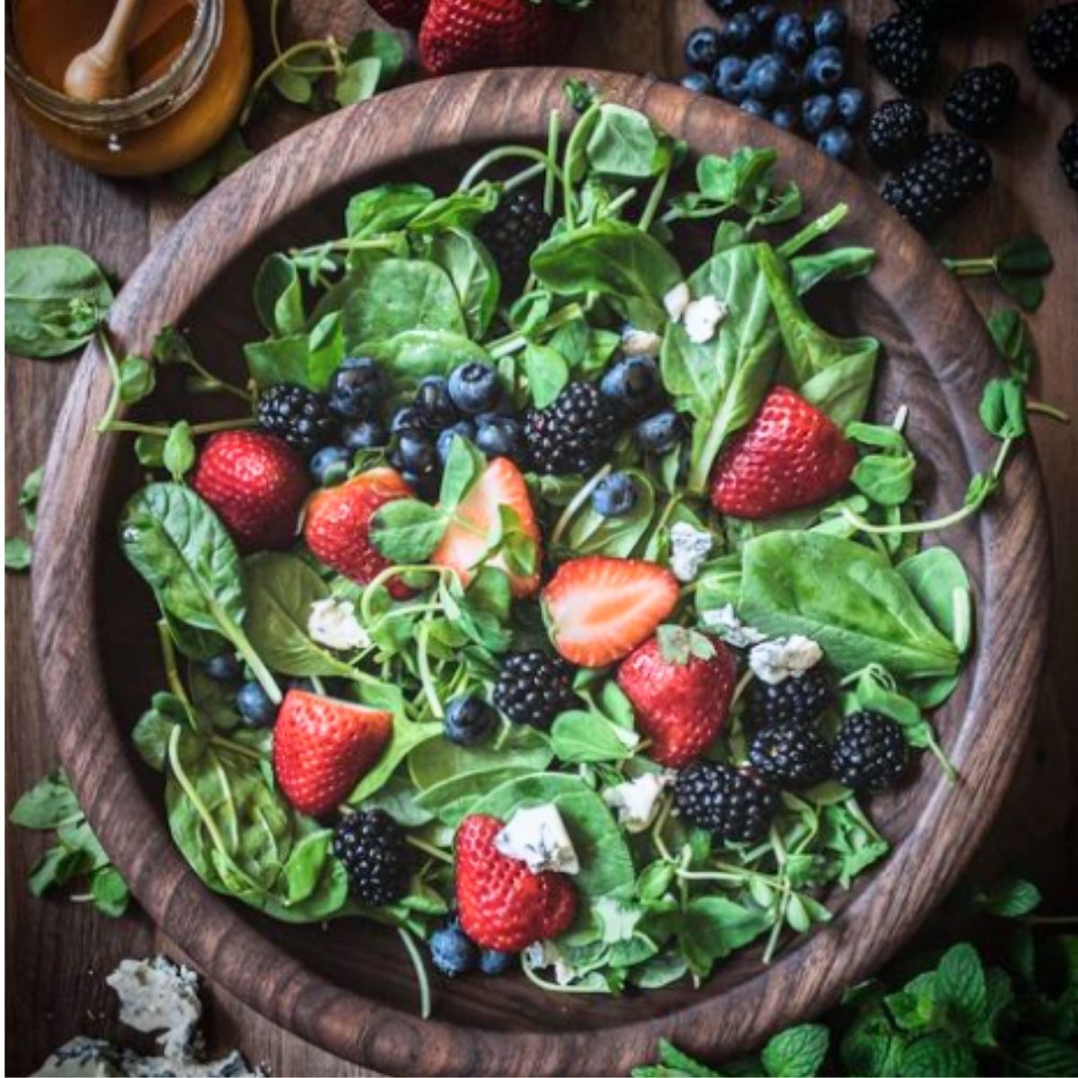 Mixed green salad with berries and cheese in a wooden bowl.