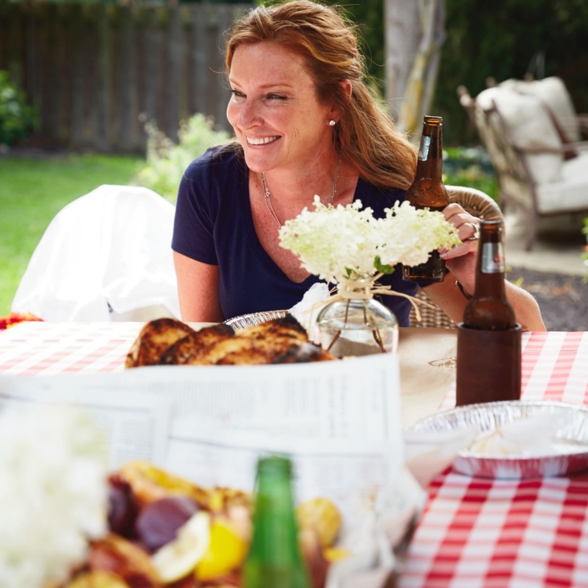 Pretty redhead at a table, smiling, and the table is filled with shrimp oil and beer.