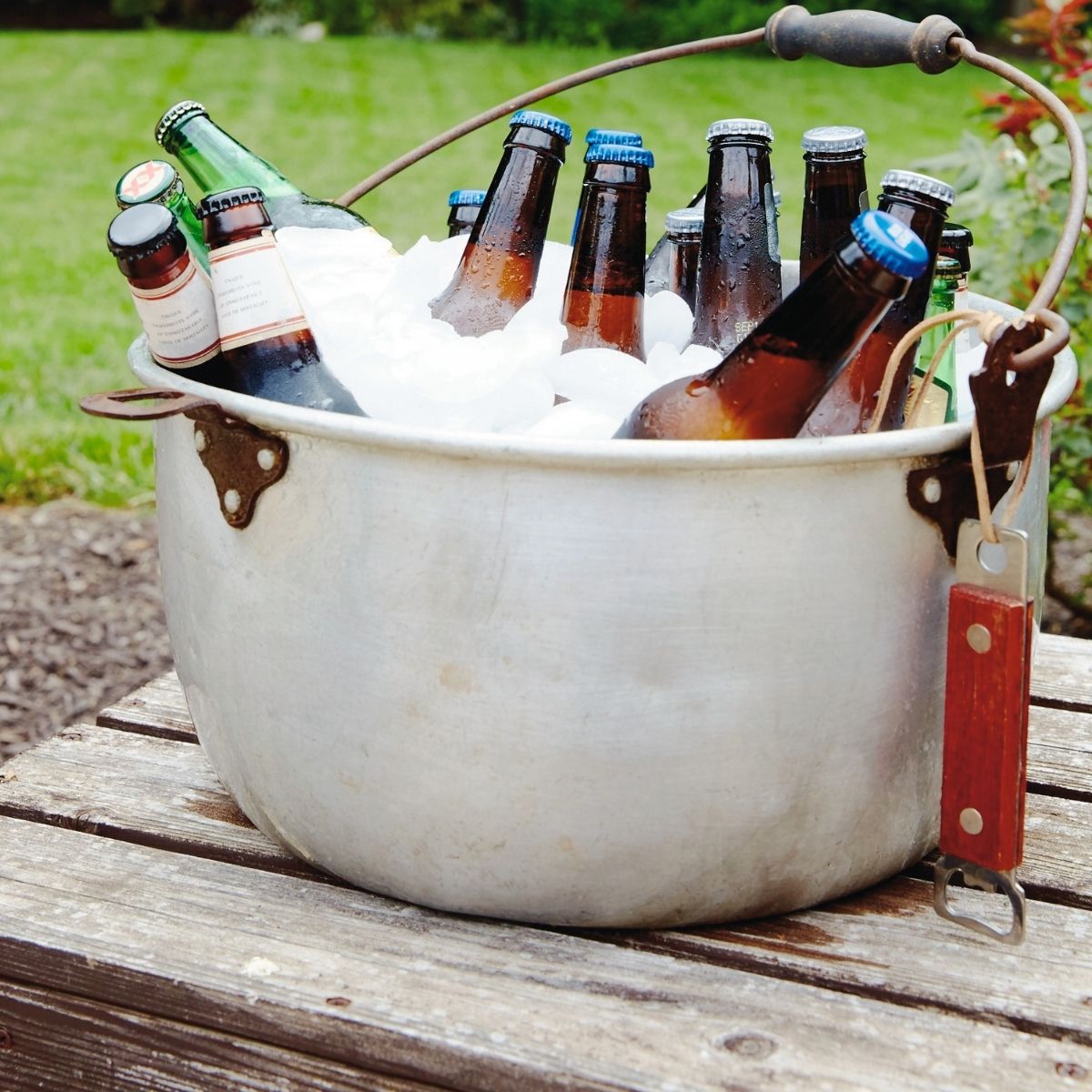 Bear in a old bucket filled with ice on a wood table with a bottle opener, hanging off the bucket.