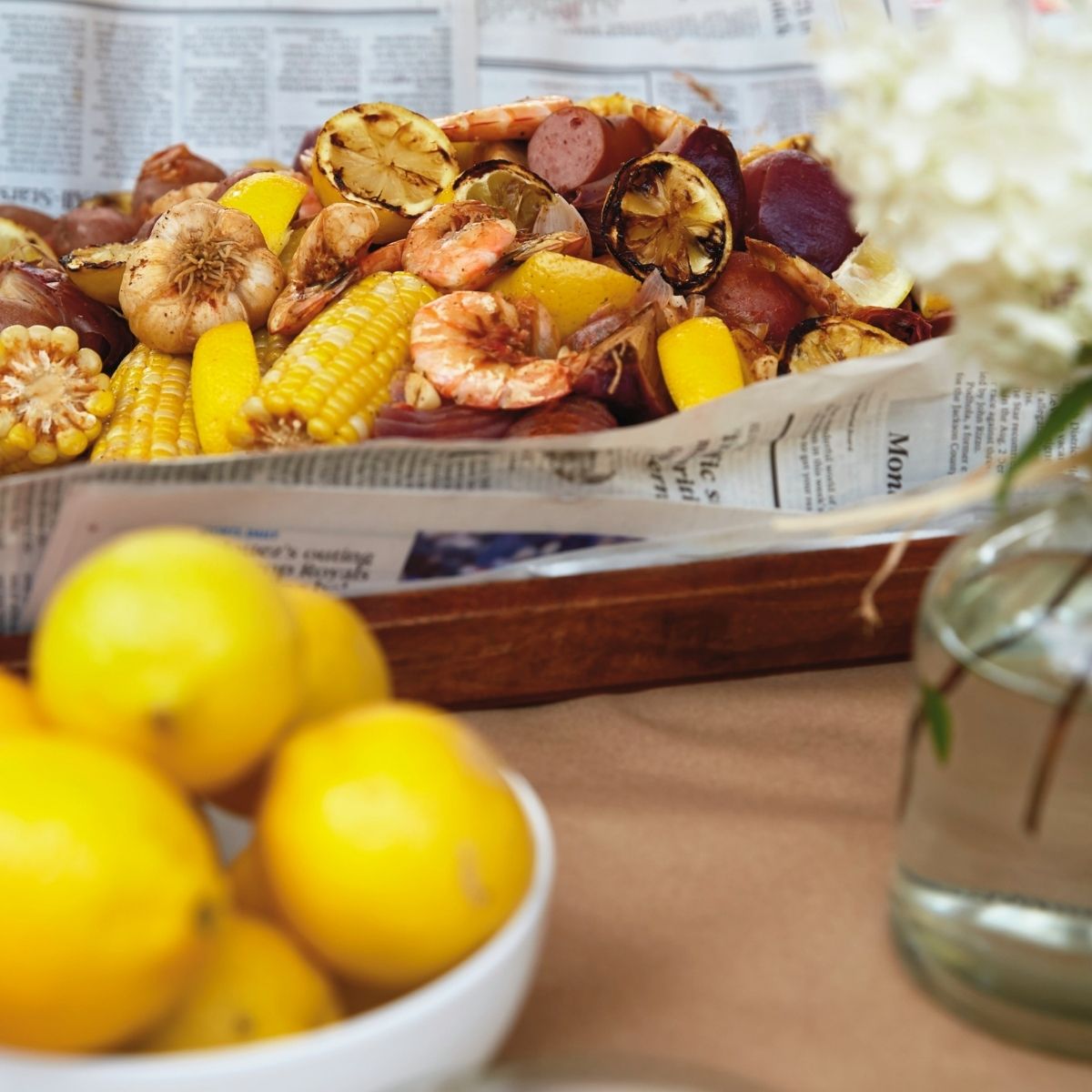 Lemons in a bowl in front of a shrimp boil with in a newspaper covered tray