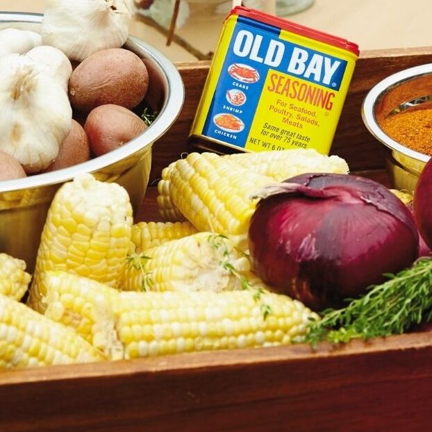 Shrimp, boil ingredients, prepped, and placed in a wood tray sitting on a red and white checkered tablecloth table.