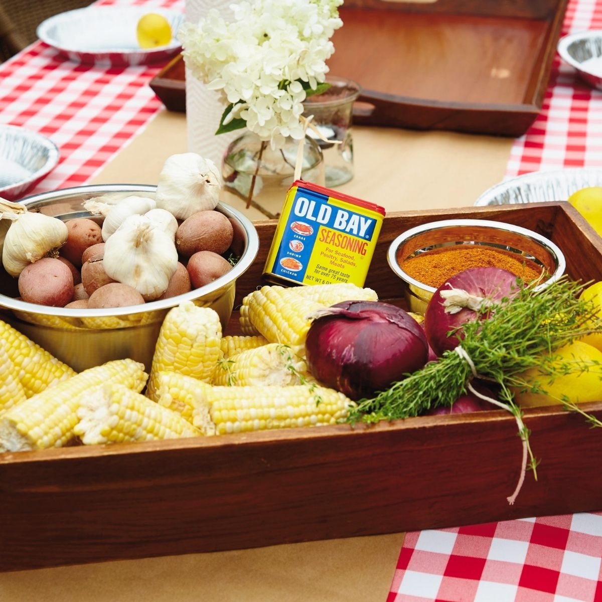 Shrimp, boil ingredients, prepped, and placed in a wood tray sitting on a red and white checkered tablecloth table.