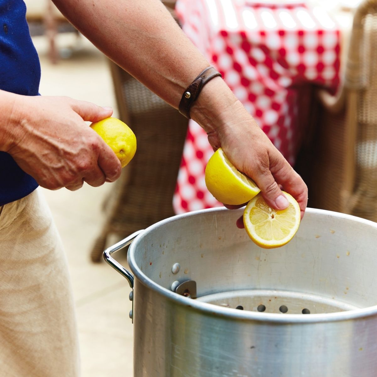 A shrimp boil pot with lemons and potatoes, be added to it with a red and white checkered tablecloth in the background.